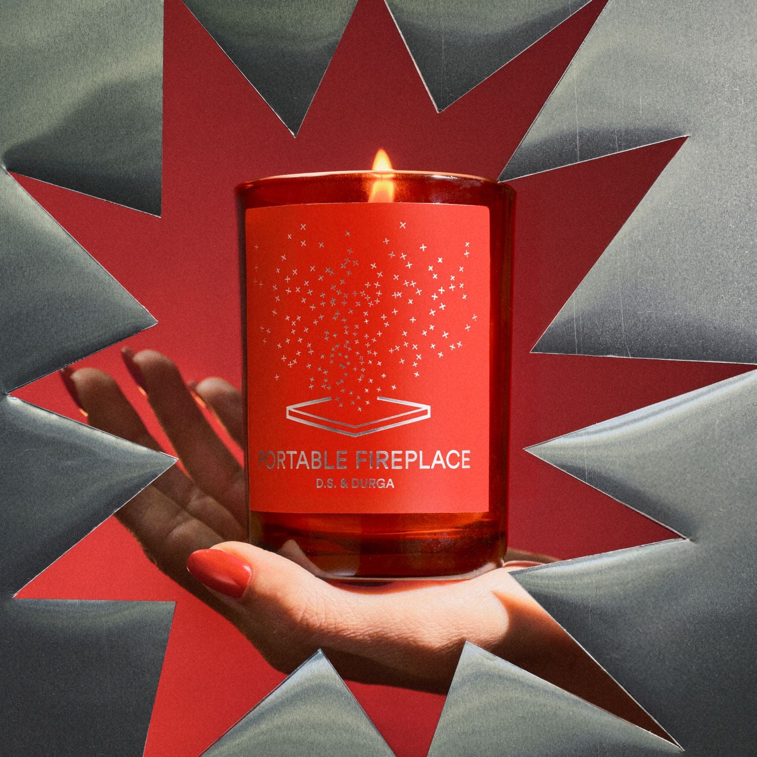 Red candle labeled 'Portable Fireplace' held by a hand against a geometric background