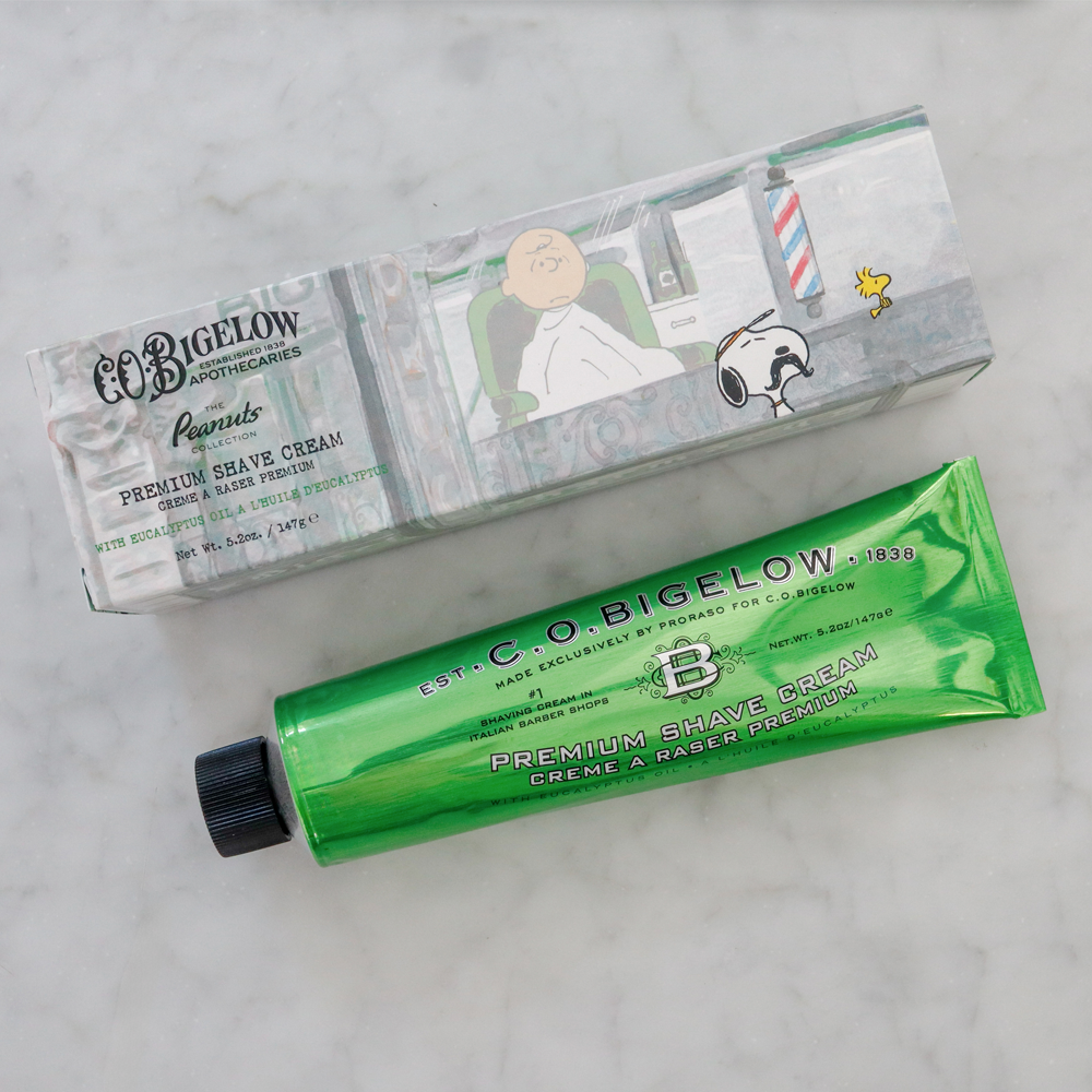 Peanuts® x C.O. Bigelow Premium Shave Cream and packaging on a marble surface background