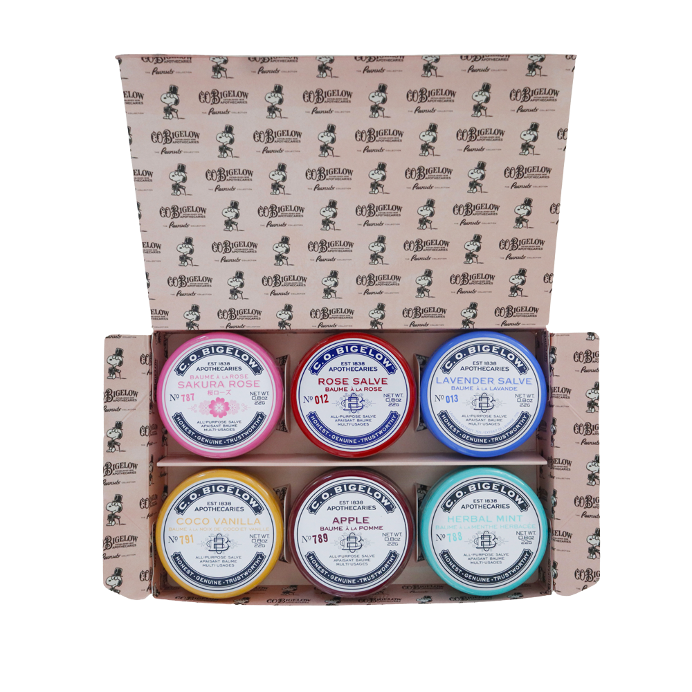 Peanuts® x C.O. Bigelow The Salve Series tins in open packaging on a white background