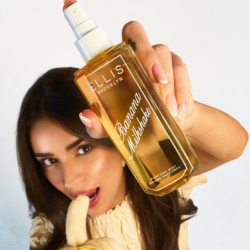 Person holding a bottle of Ellis Brooklyn Banana Milkshake perfume with a banana in front of a white background