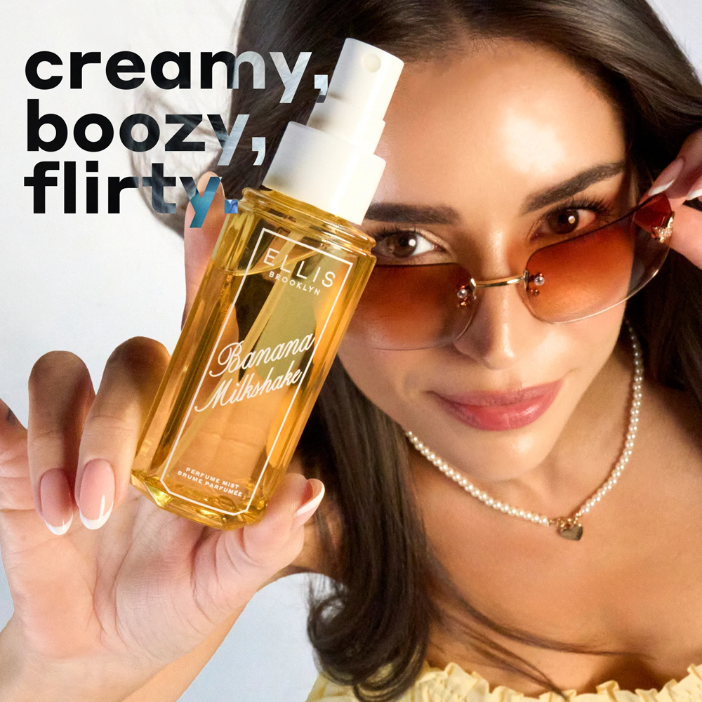 Woman holding a bottle of Ellis Brooklyn Banana Milkshake perfume with text 'creamy, boozy, flirty' on a white background.