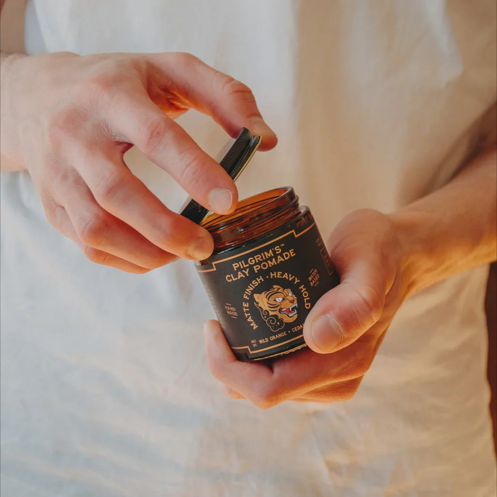 Hands holding open jar of Pilgrim's Clay Pomade.
