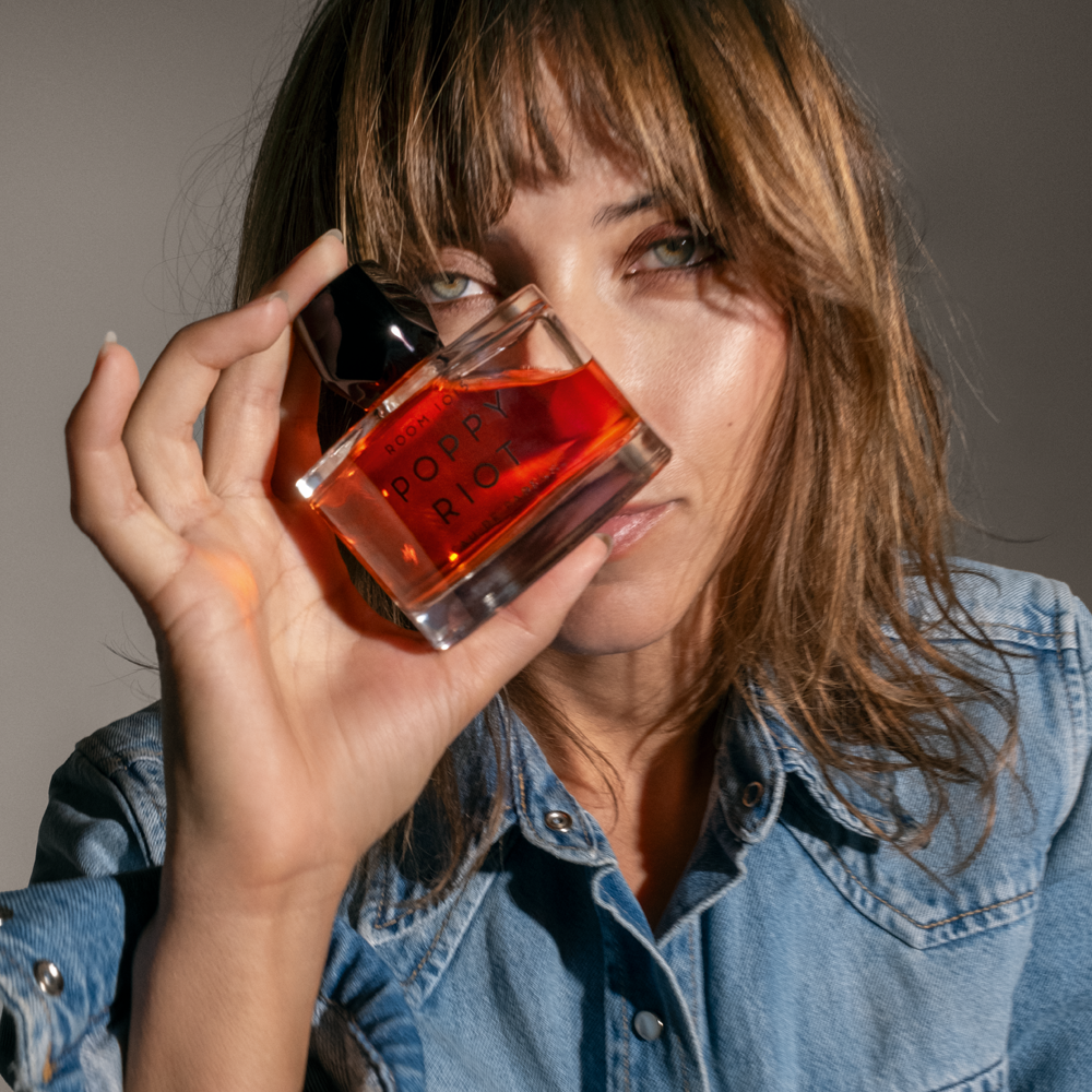 Woman holding Room 1015 Poppy Riot Eau De Parfum product in front of her face