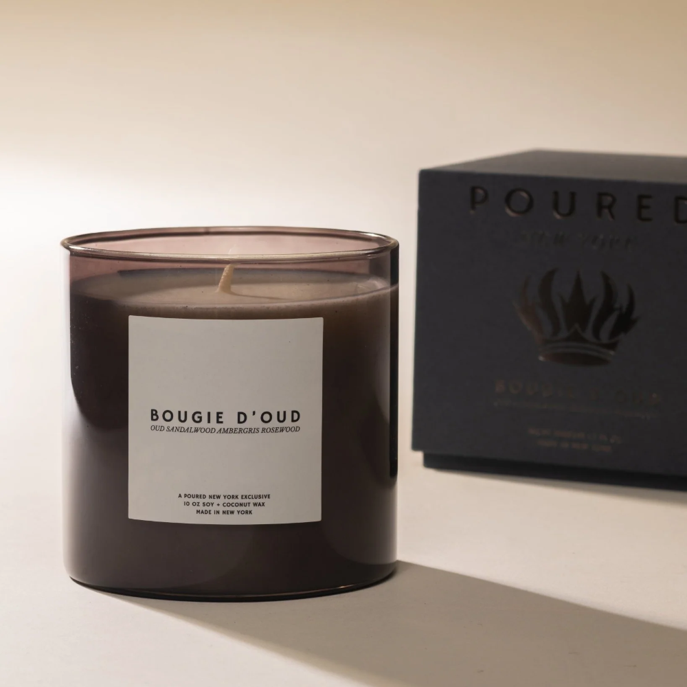 Candle labeled 'Bougie D'Oud' with a 'POURED' box in the background on a light surface.