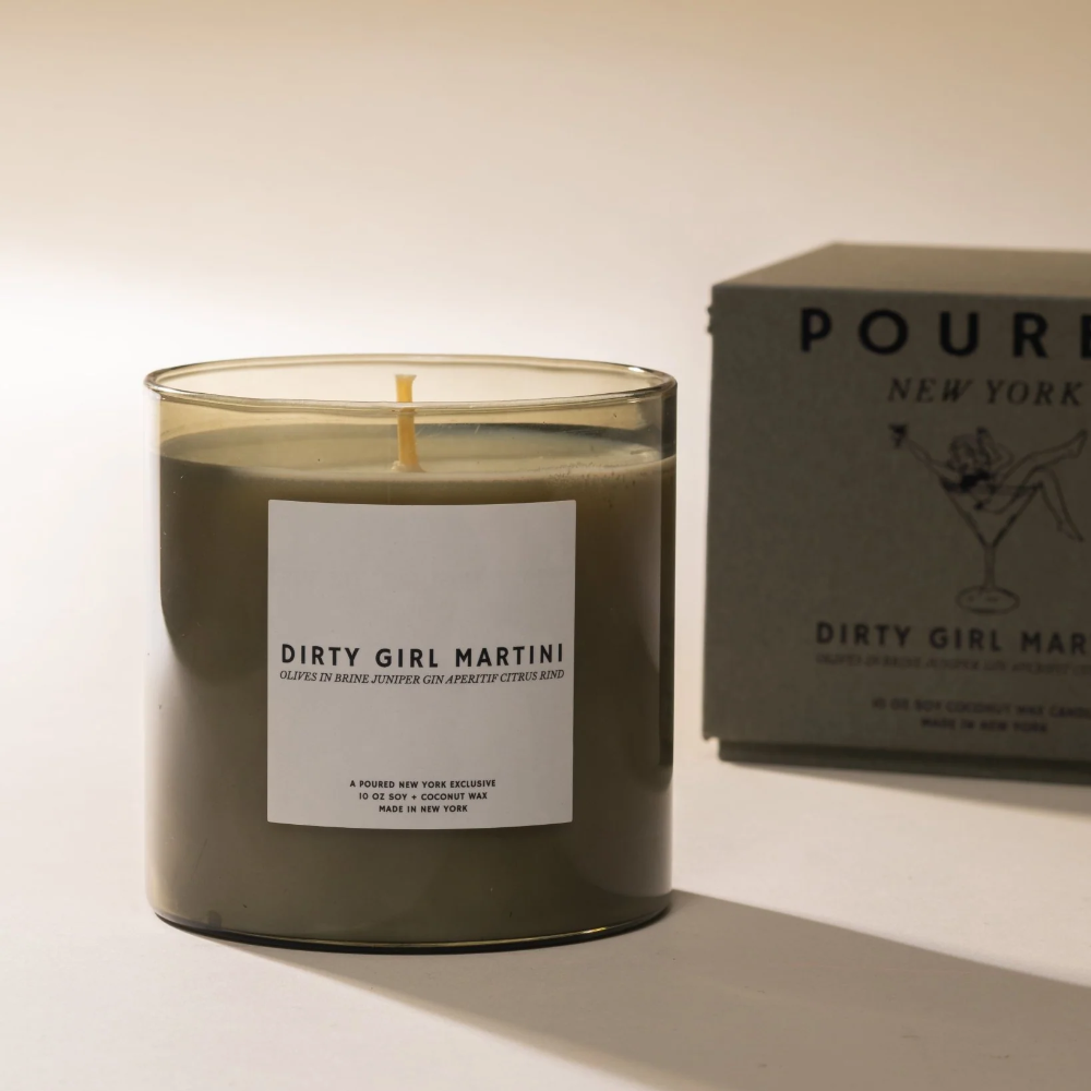Candle labeled 'Dirty Girl Martini' with a box in the background on a light surface.