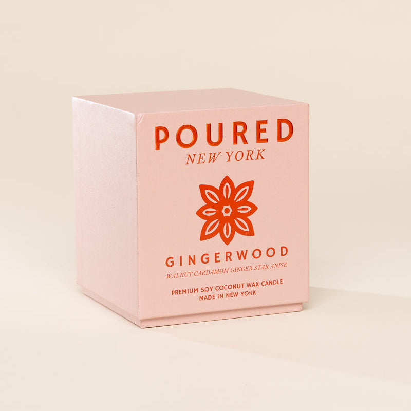A light pink cube-shaped product box for a Poured New York Gingerwood candle, featuring an orange floral logo and text, set against a solid cream background.