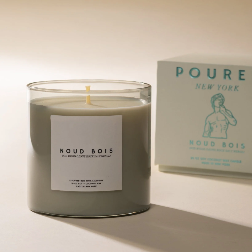 Candle labeled 'Noud Bois' with packaging in the background on a light background