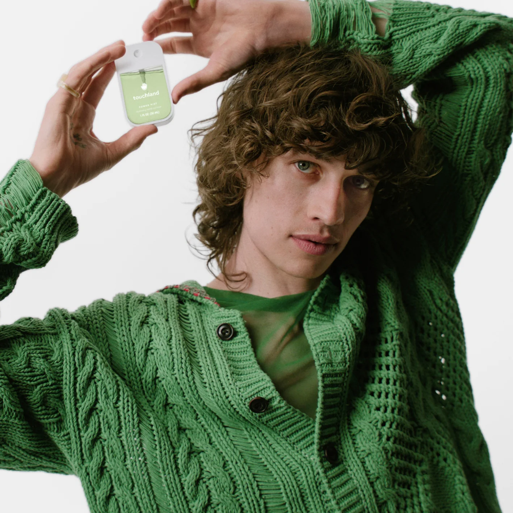 Person wearing a green knitted sweater holding Touchland product.