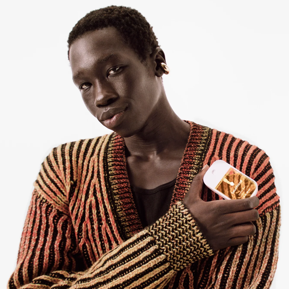 Person wearing a striped sweater holding Touchland product on a white background