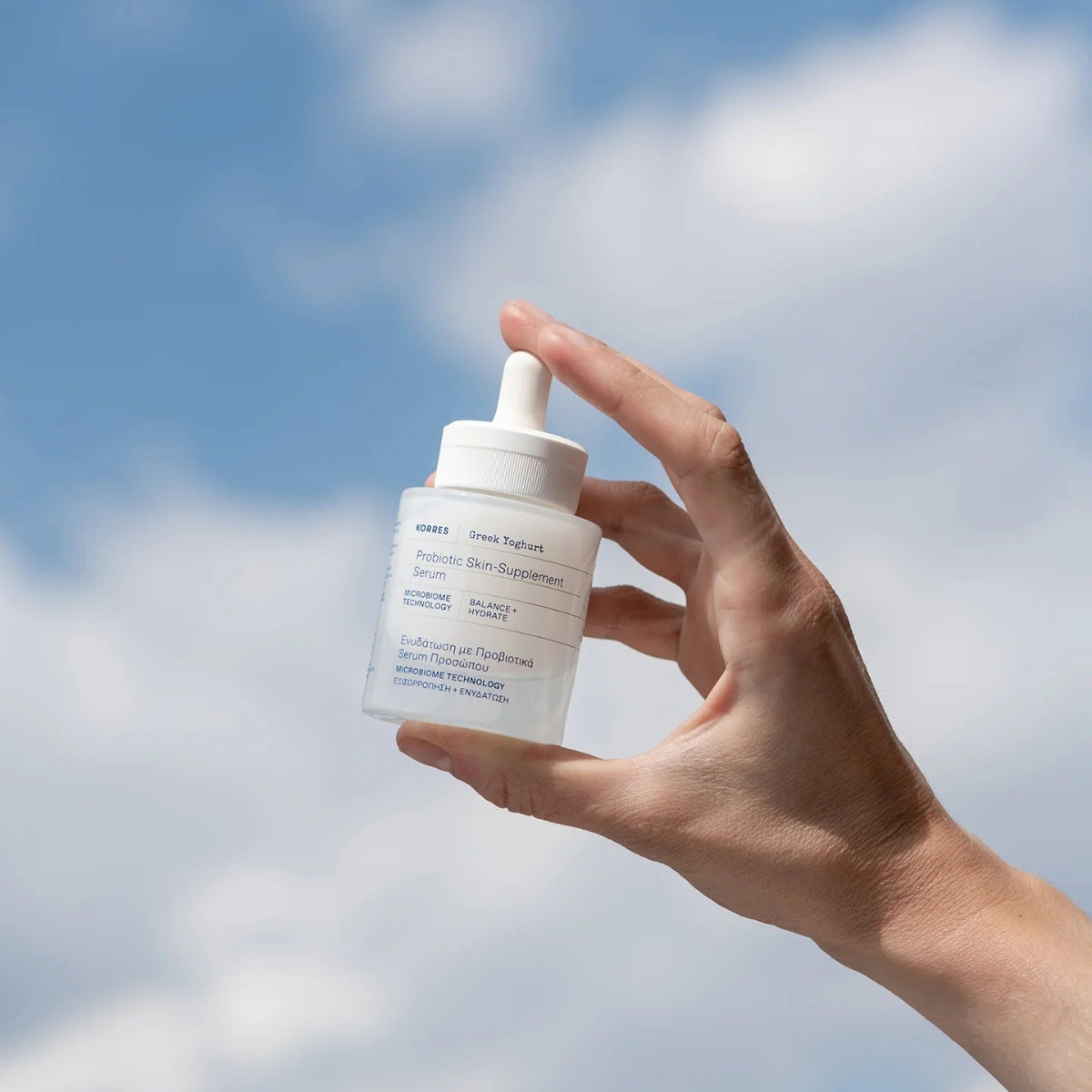 Hand holding a skincare dropper bottle against a blue sky background