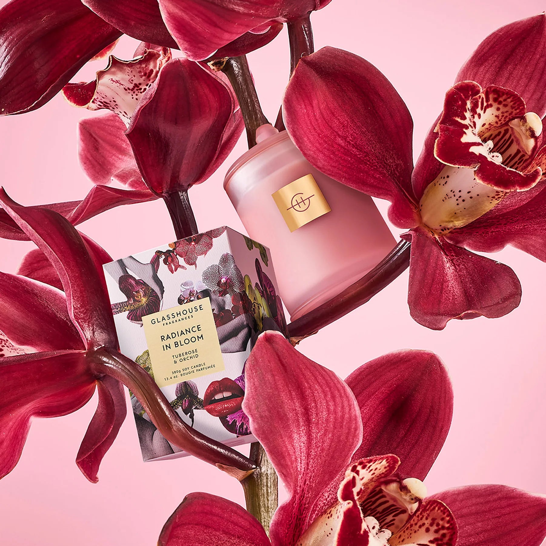 Pink candle and product packaging surrounded by red orchids on a pink background
