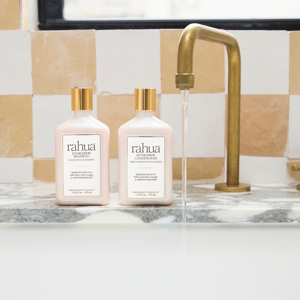 Two rahua  bottles on a bathroom counter with a gold faucet.