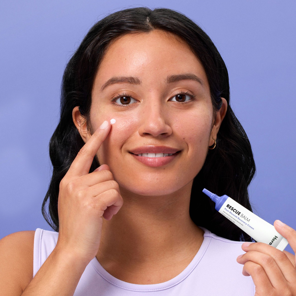 Woman applying skincare product to her face with a purple background