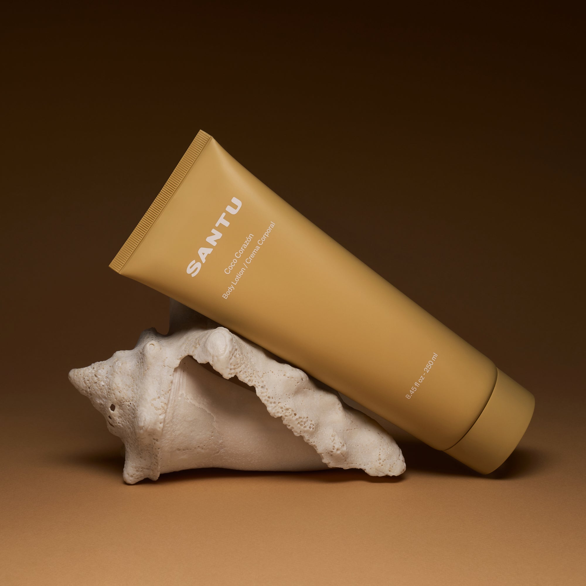 Beige tube of Santu body cream on a white shell against a brown background