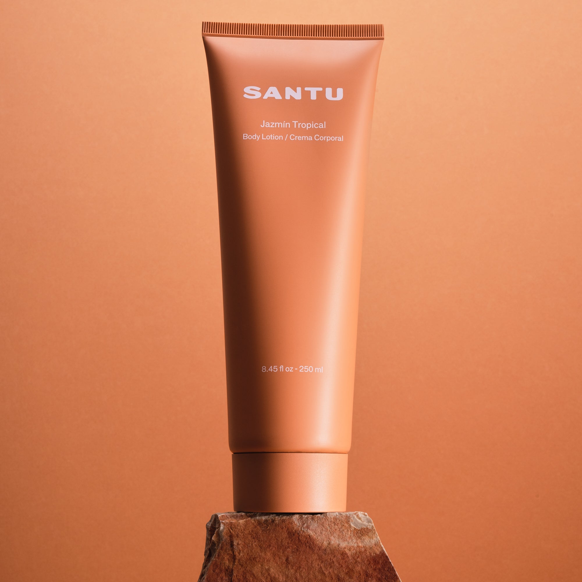 Santu body lotion tube on a rock in front of a coral background