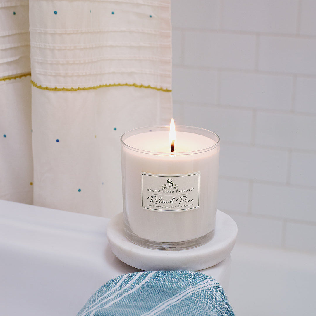 Roland Pine Candle on a coaster with a label, next to a blue towel on a white surface.