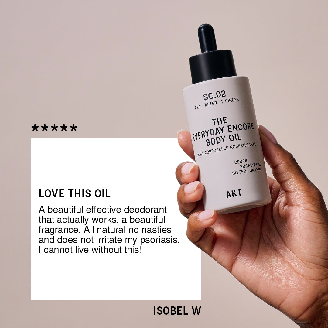 Hand holding a bottle of 'The Everyday Encore Body Oil' with a beige background and review text.