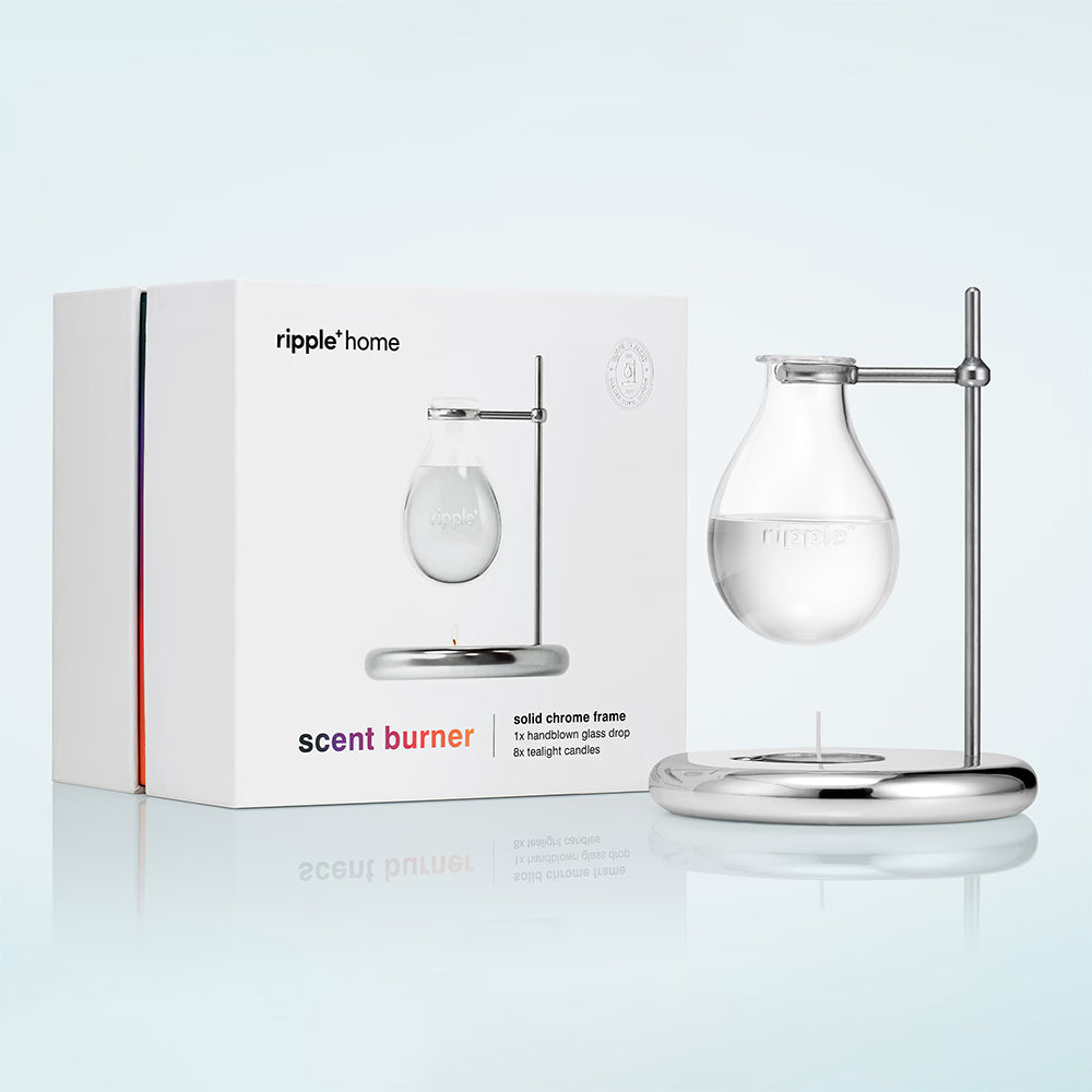 Scent burner with chrome frame and glass container next to its packaging box on a white background