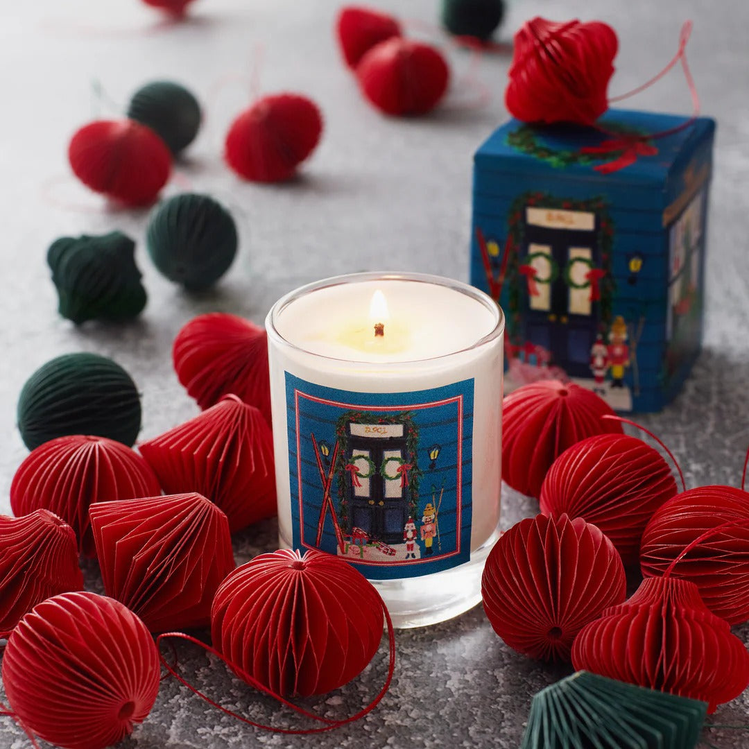 Roland Pine Candle with decorative label surrounded by red and green paper balls on a gray surface