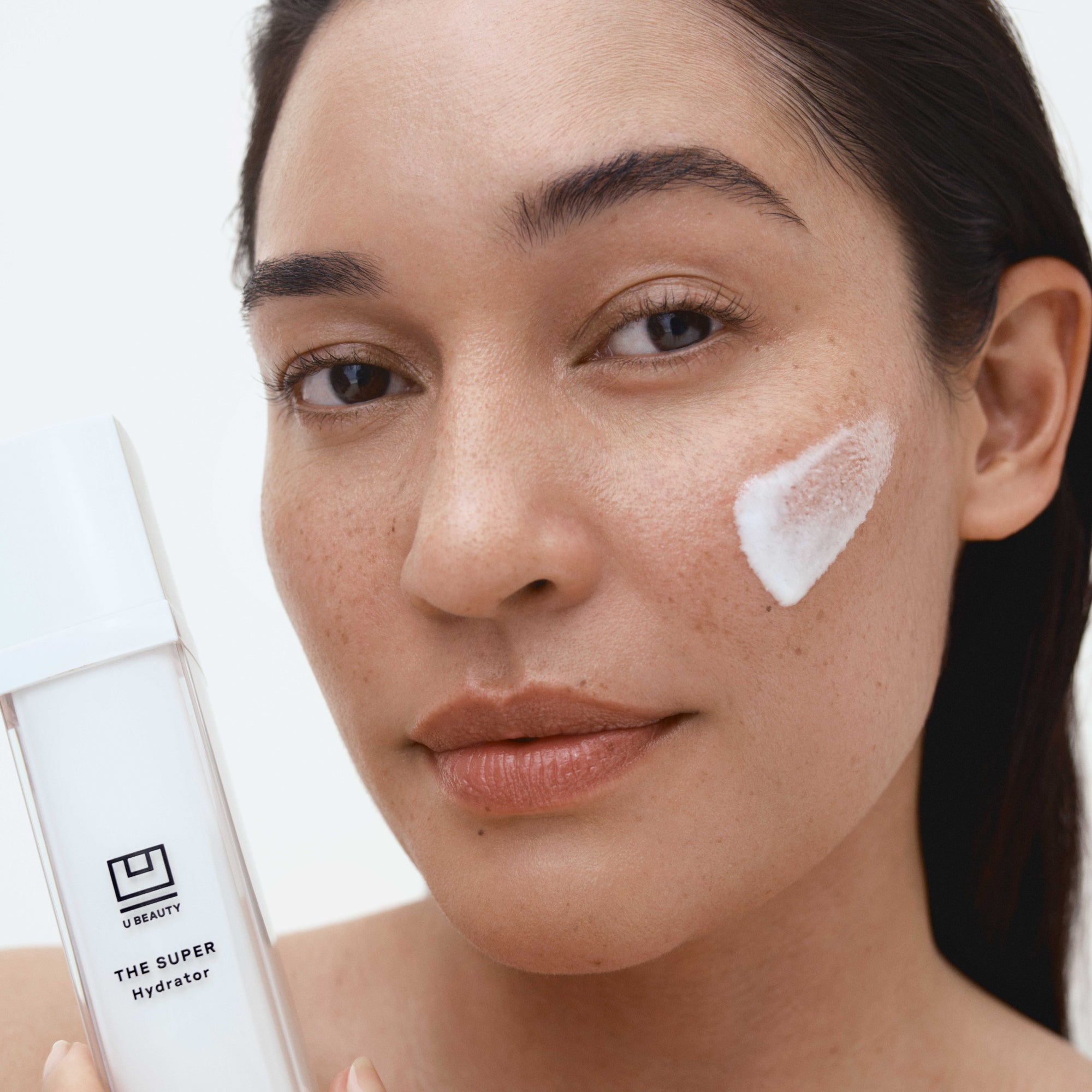 Woman applying skincare product with 'U Beauty' bottle in the background
