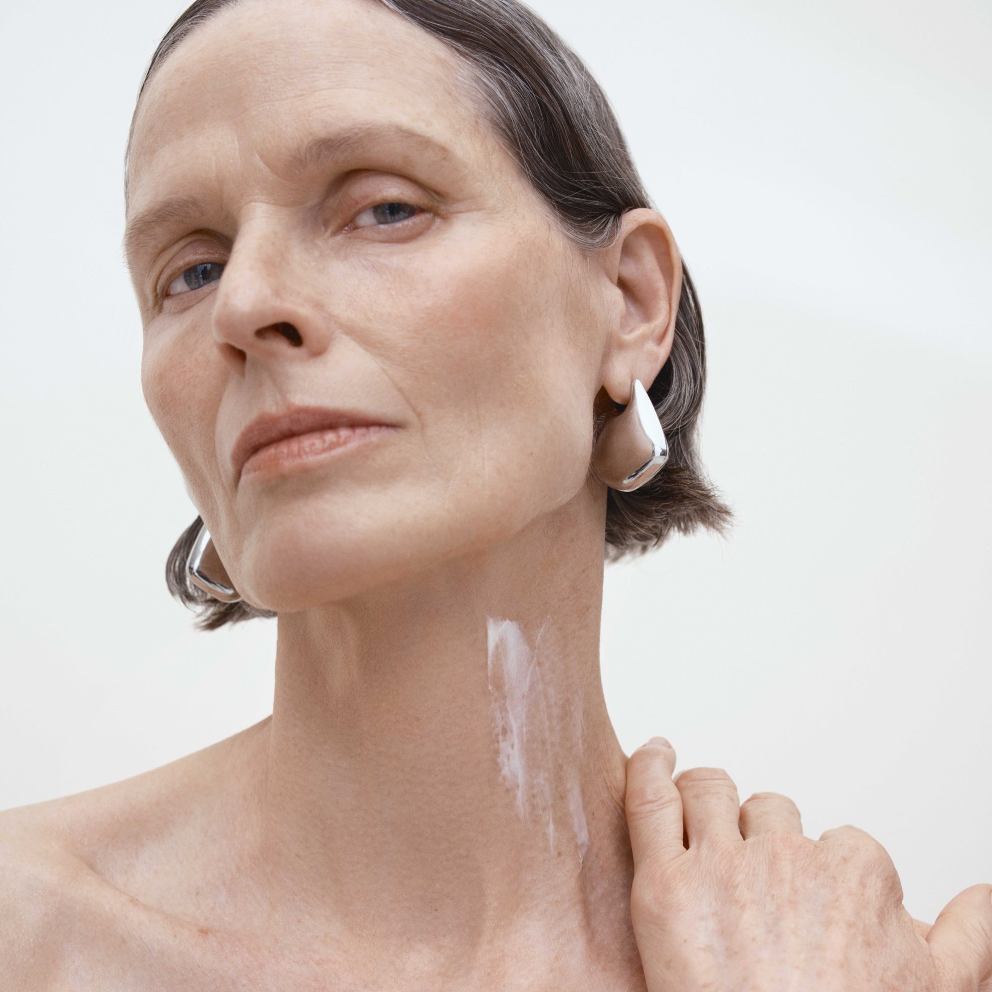 Woman applying a skincare product to her neck with a white background