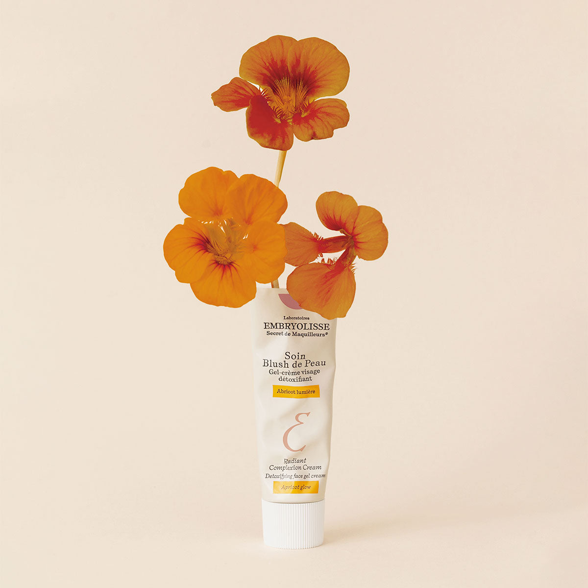 Embryolisse Radiant Complexion Cream in Apricot Glow with orange flowers coming out the top of the bottle. 