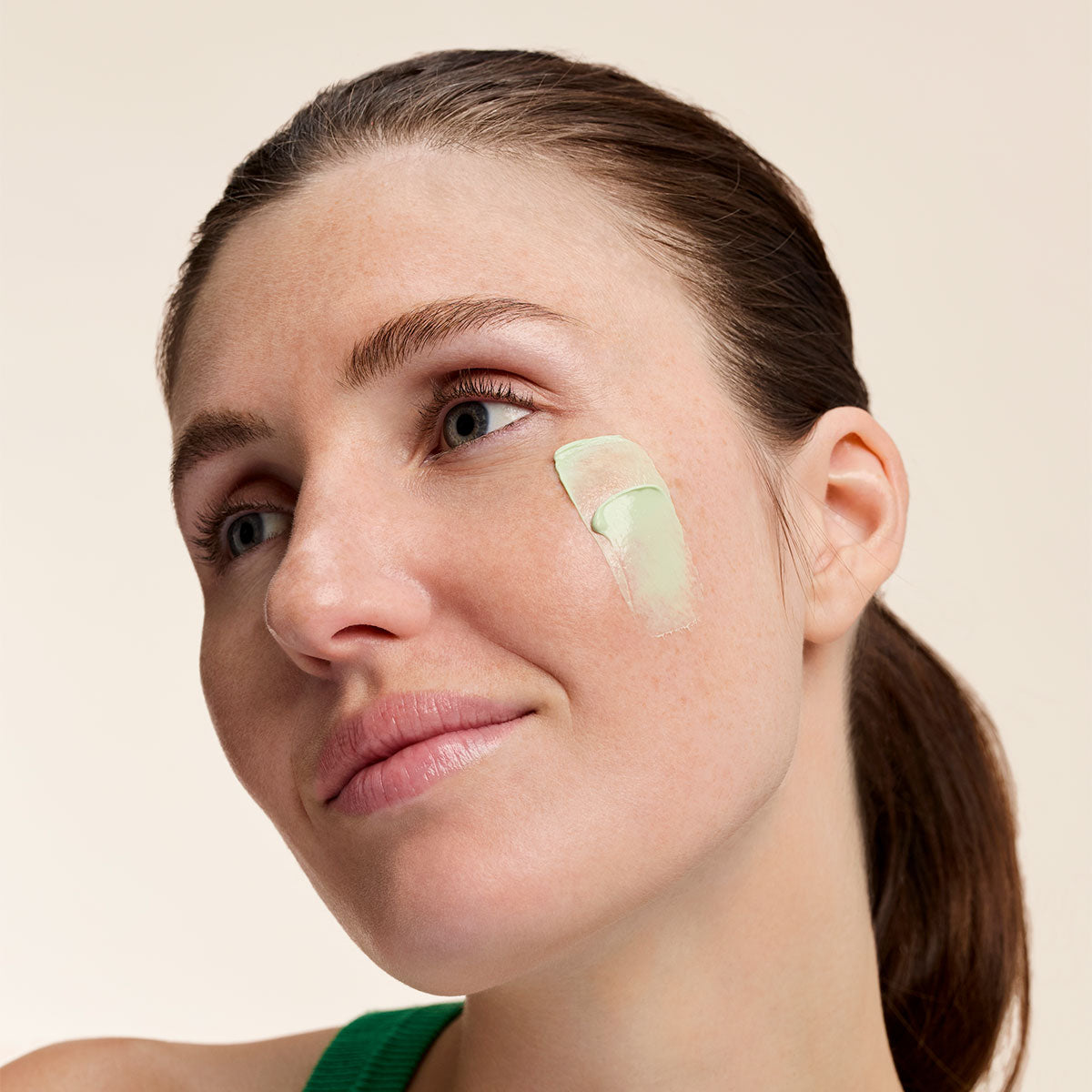 Woman wearing a swatch of Embryolisse SOS Corrective Cream on her cheek.