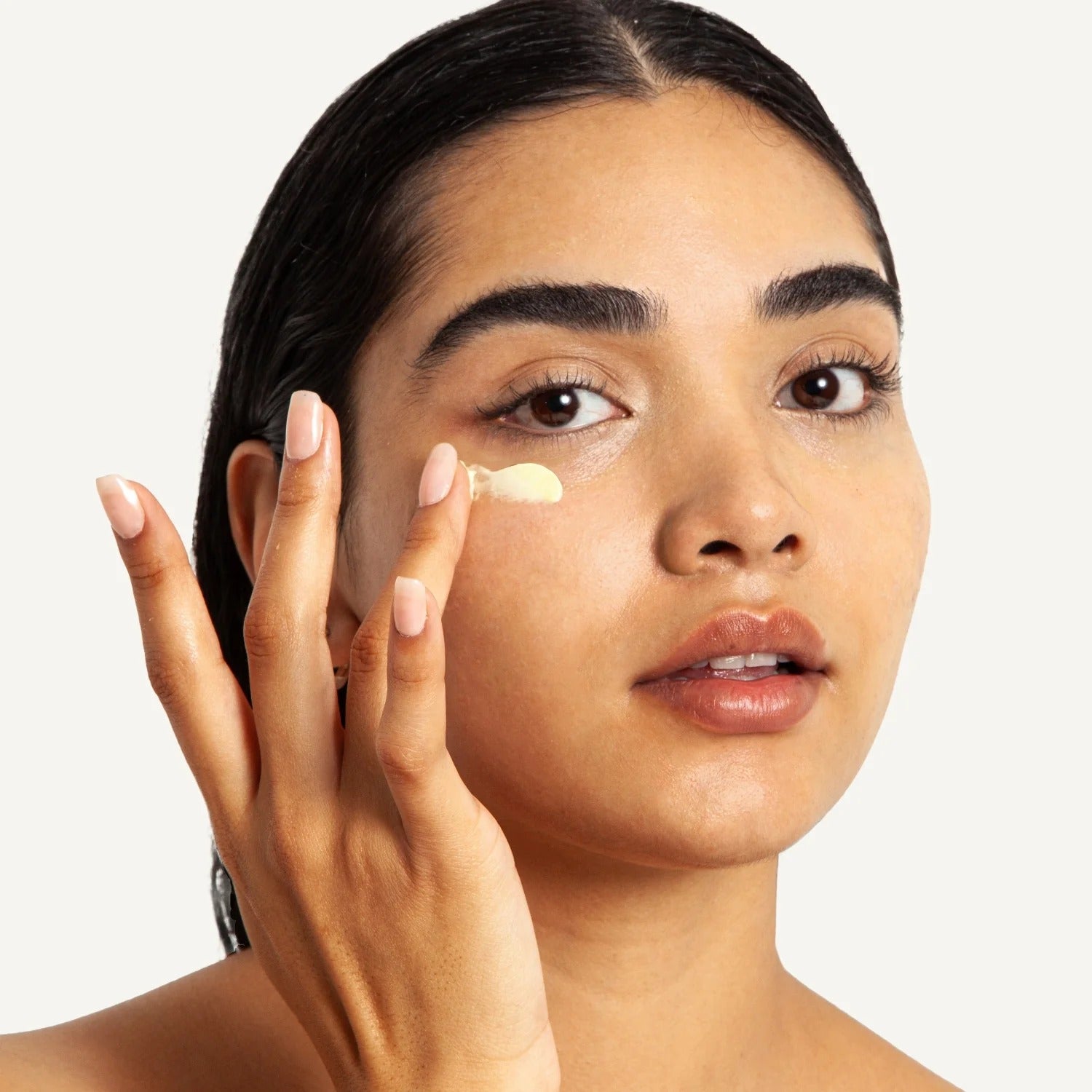 Woman applying cream to her face with a neutral background