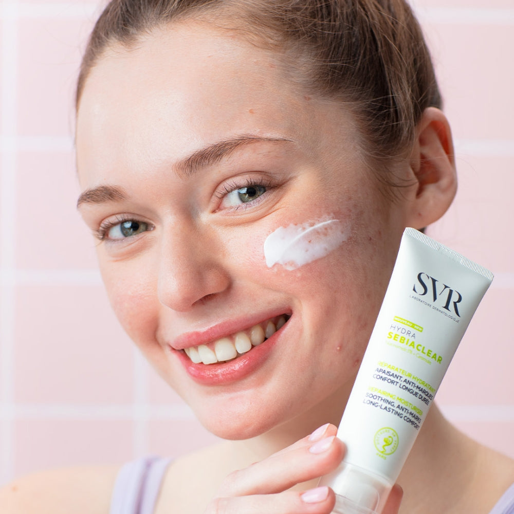 Woman applying cream to her face with SVR Sebiaclear Hydra Cream on a pink background