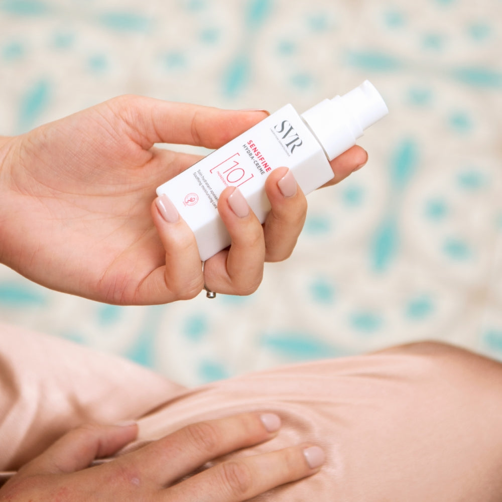 Hand holding a white bottle labeled SVR  Sensifine hydra cream 