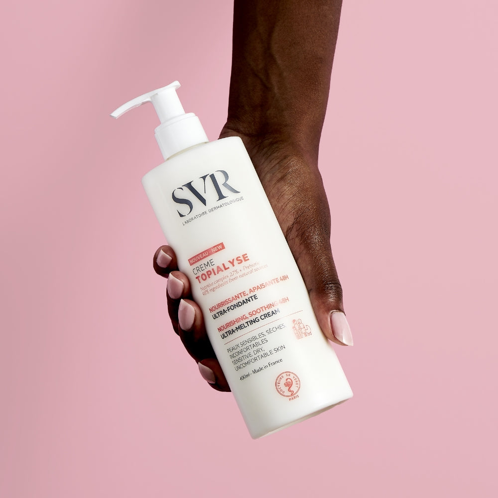 Hand holding a SVR  Topialyse creme  against a pink background