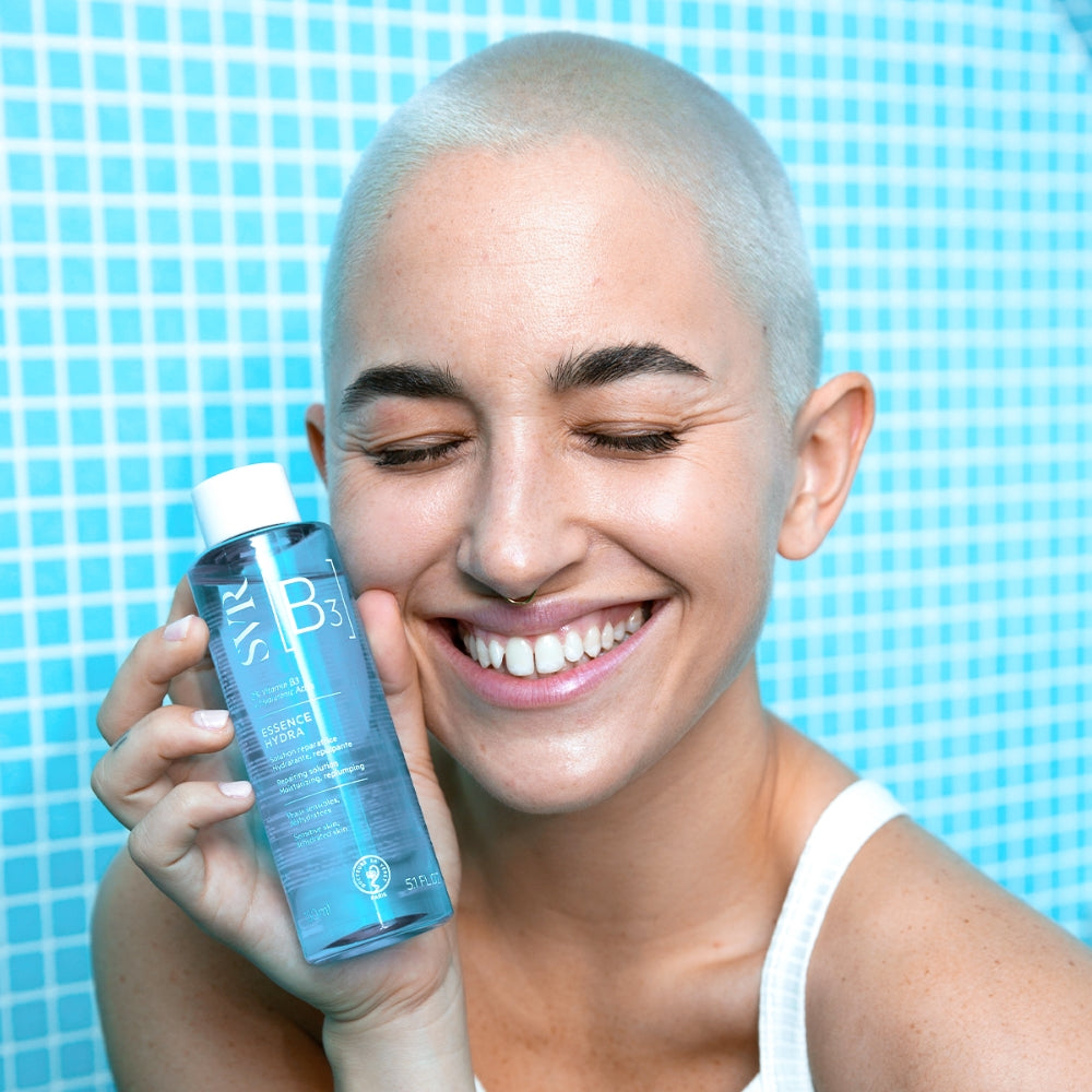 Person holding a SVR B3 Hydra Essence bottle with a white cap against a blue tiled background