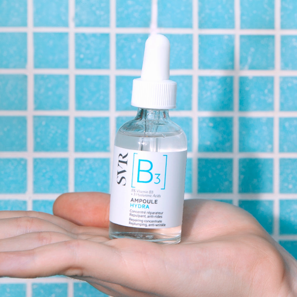 Bottle of SVR B3 Repairing Concentrate ampoule held in a hand with a blue tiled background
