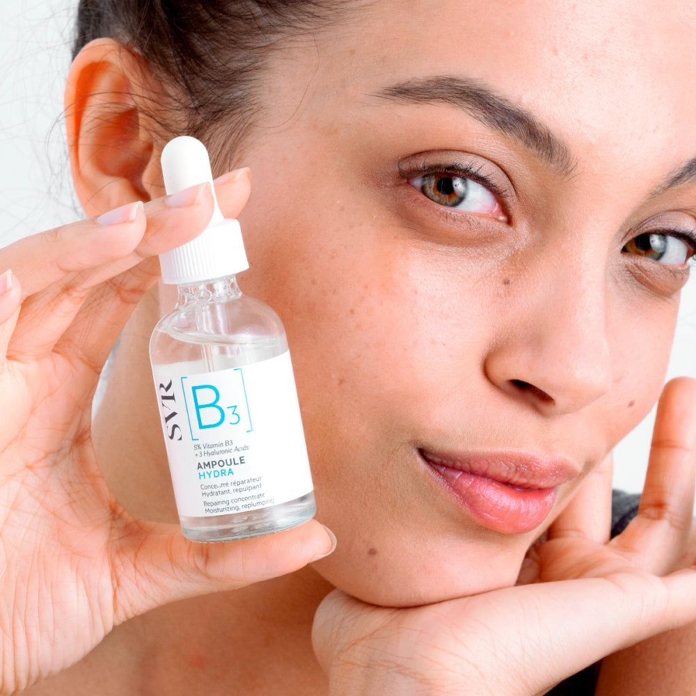 Woman holding a bottle of SVR B3 Repairing Concentrate Ampoule Hydrating Serum close to her face.