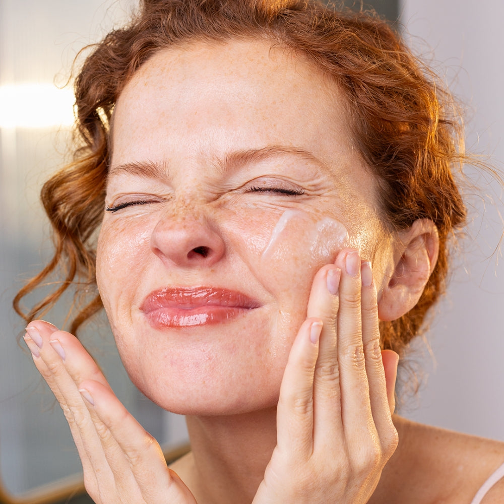 Woman applying Sensifine cleansing cream to her face with a neutral background
