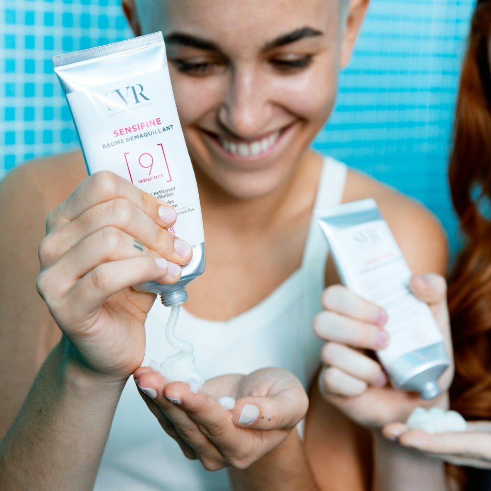 Woman holding two SVR Cleansing Balm in a bathroom setting.