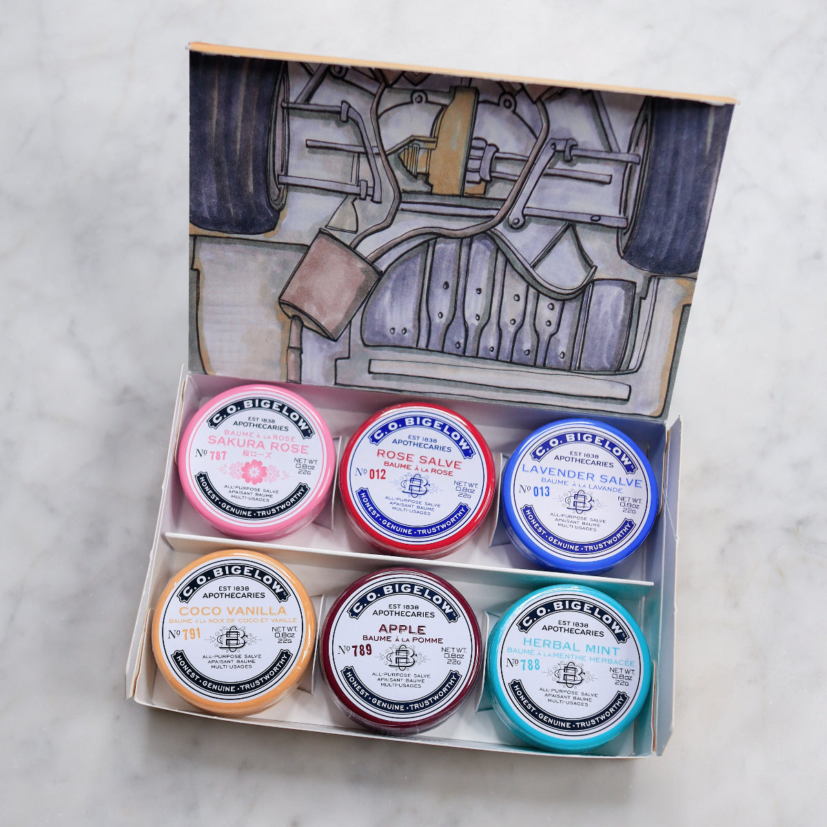 Set of six small containers with lids in a decorative box on a light gray background