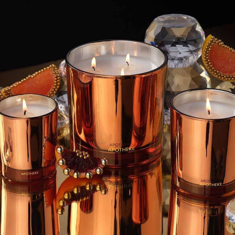 Three rose gold candles with 'Apotheke' branding on a reflective surface.