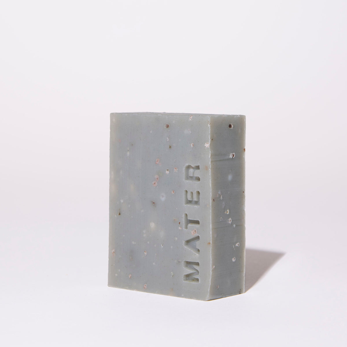 A rectangular bar of gray soap with embedded small specks and the brand name 'MATER' embossed vertically on the front, photographed on a clean white background.