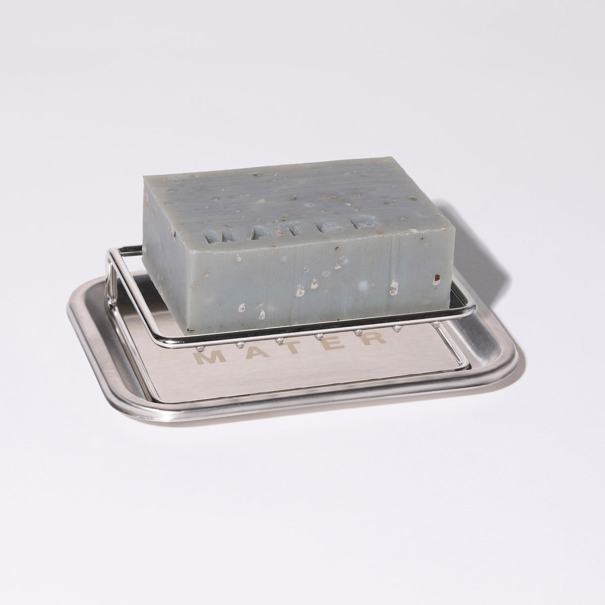 A rectangular bar of speckled gray soap resting on a small silver metal soap dish, photographed on a clean white background.