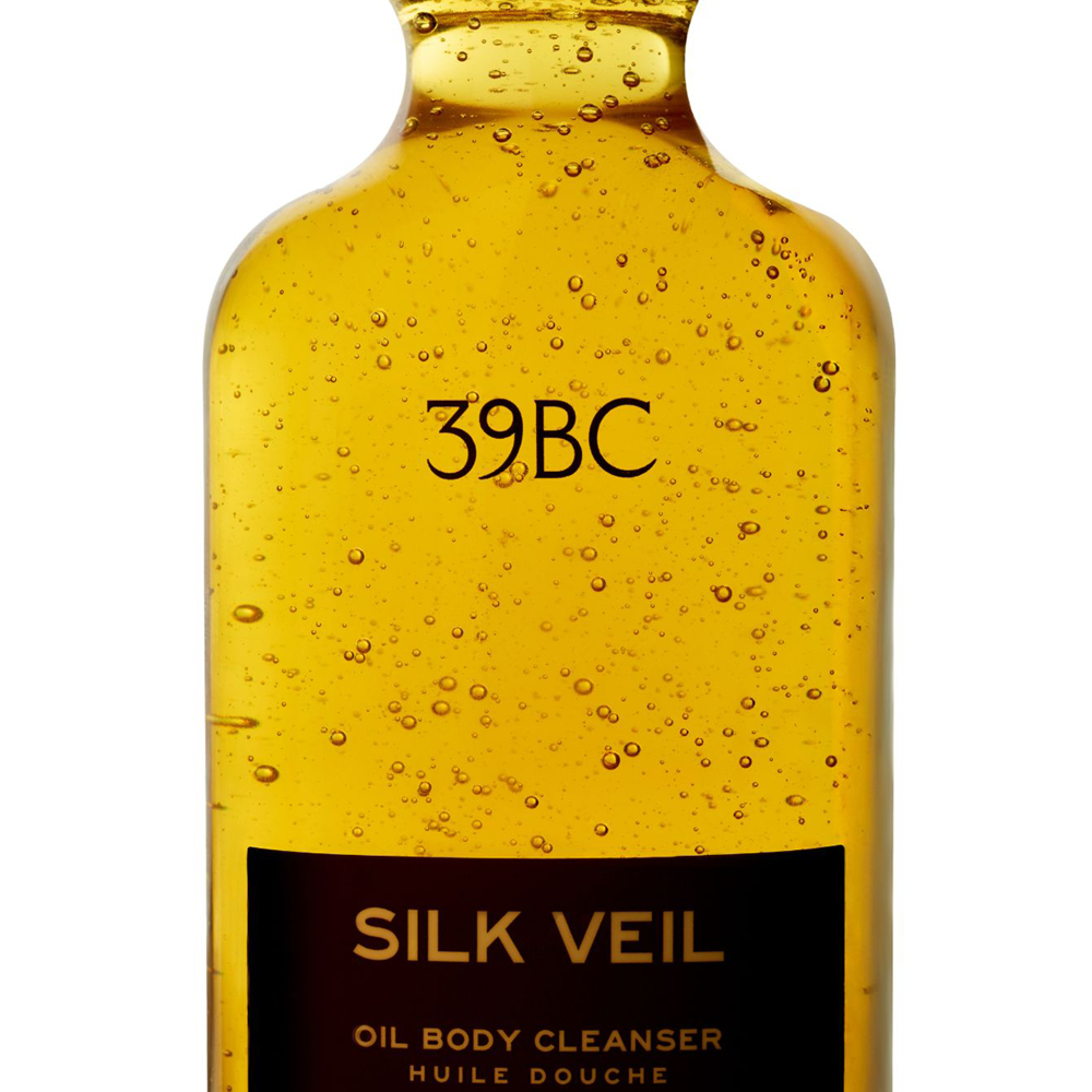 A bottle of 39BC Silk Veil Oil Body Cleanser filled with golden yellow oil and suspended bubbles, featuring a black label with gold lettering, set against a plain white background.