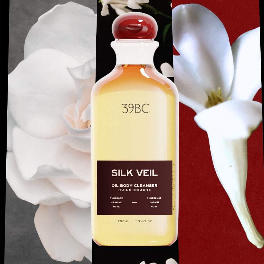 A bottle of 39BC Silk Veil Oil Body Cleanser, featuring a pale yellow liquid and a dark brown label, set against a split background of white flowers on the left and a red background on the right.