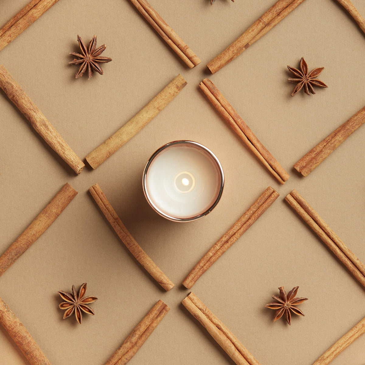 Candle surrounded by cinnamon sticks and star anise on a beige grid background