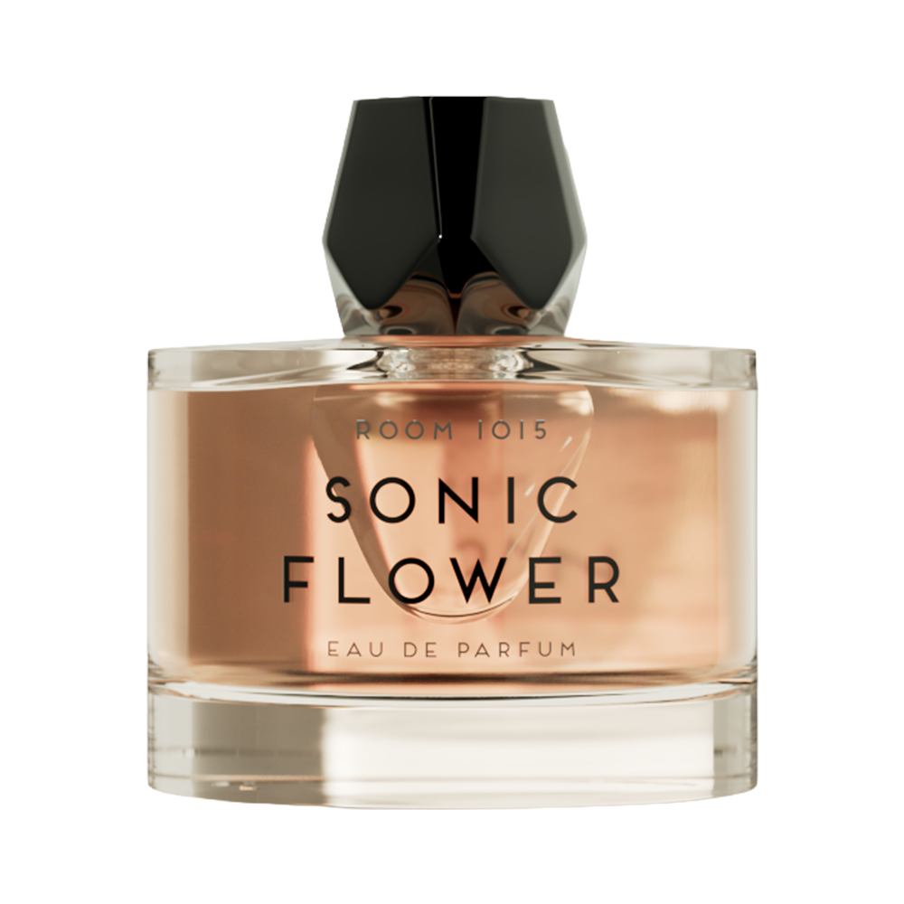 A bottle of Sonic Flower Eau de Parfum by Room 1015, featuring a clear glass bottle with a warm peach-pink liquid, a black faceted cap, and black lettering on the front, set against a solid white background.