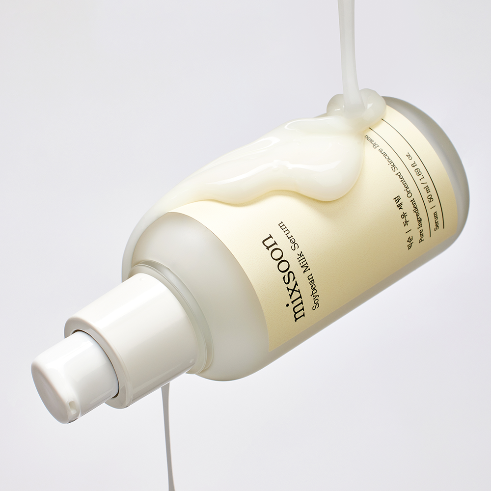 A bottle of Mixsoon Serum Milk suspended against a light gray background, with thick creamy serum dripping from the top and around the bottle.