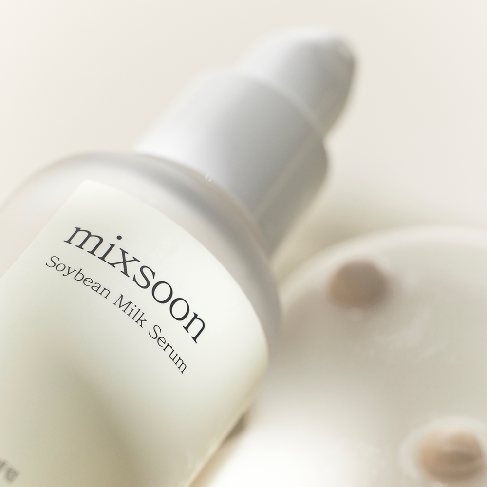 A close-up of a mixsoon Soybean Milk Serum set against a soft cream background with a blurred circular product container in the foreground.