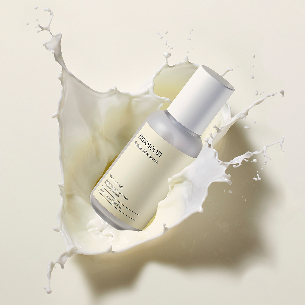 Bottle of mixsoon Soybean Milk Serum inside a dramatic splash of white liquid on a warm cream background.