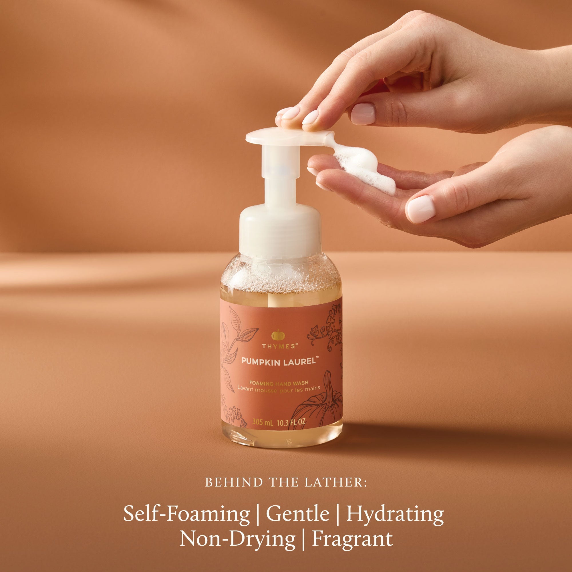 Hand holding a pump bottle of 'Pumpkin Laurel' soap with a brown background