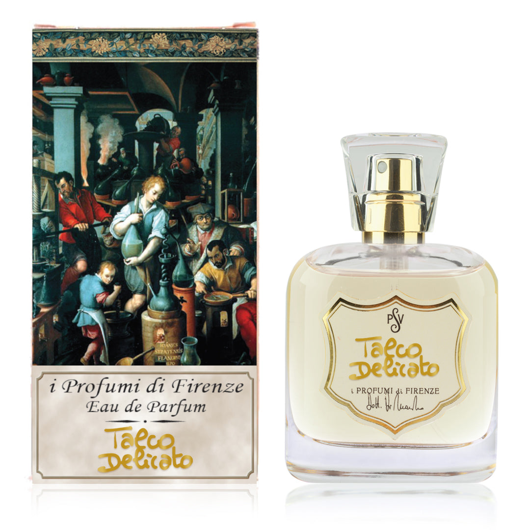 A bottle of Tacco Delicato Eau de Parfum next to its retail box. The clear glass bottle contains a pale yellow liquid and features a gold spray cap and a gold shield-shaped label with the brand name 'i Profumi di Firenze'.