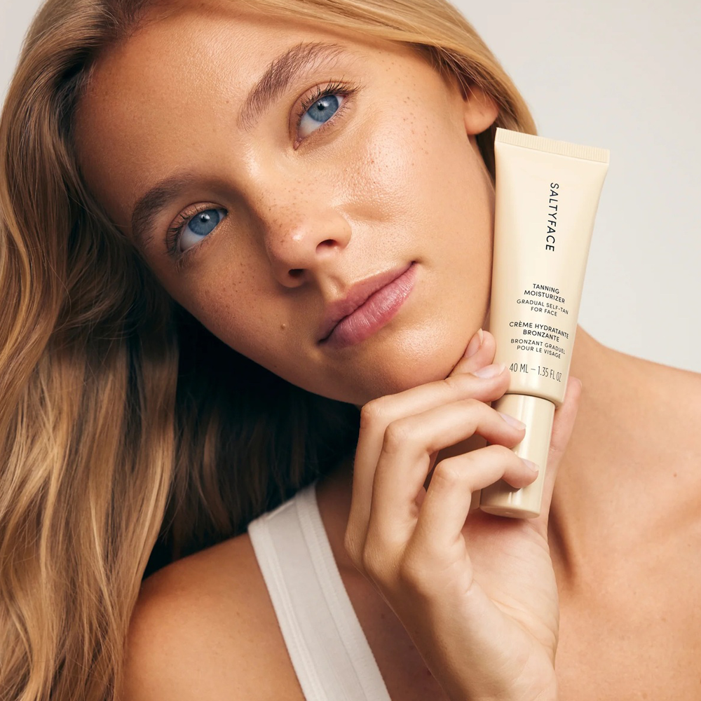 Woman holding a tube of SaltLife skincare product against a neutral background